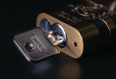 ein ABUS IRON ROCK 83/45 schräg von der Unterseite mit eingestecktem Schlüssel in der Färbung Messing mit schwarzem Hintergrund